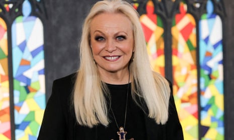 Jacki Weaver in black, in front of stained glass windows.