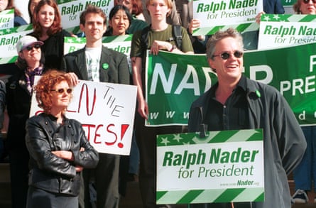 A woman and man in front of people holding green Ralph Nader signs at a rally
