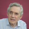 Headshot of British politician Gordon Brown in pale shirt against burgundy background