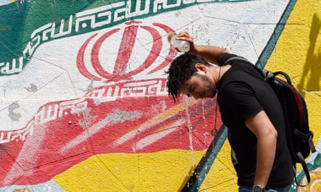 An Iranian cools off in front of a wall painting of Iran’s national flag in Tehran.