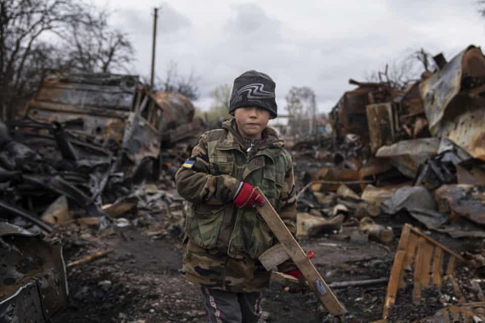 Yehor, seven, holds a wooden toy rifle next to destroyed Russian military vehicles near Chernihiv, Ukraine