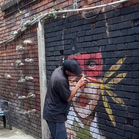 A person sprays graffiti on a brick wall.