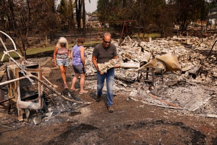 a man carries a statuette of an angel past a burned home