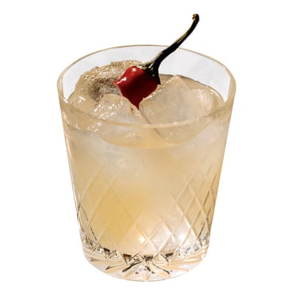 Cut-glass tumbler containing a beige-coloured cocktail with ice cubes and a red chilli garnish