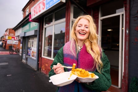 Hannah Spencer laughing and holding a portion of fish and chips outside a chip shop