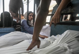 A woman mourns next to bodies wrapped in white sheets