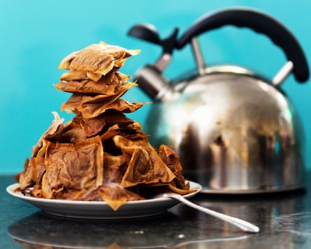 A plate piled high with crumpled, dried used teabags sits beside a kettle and spoon