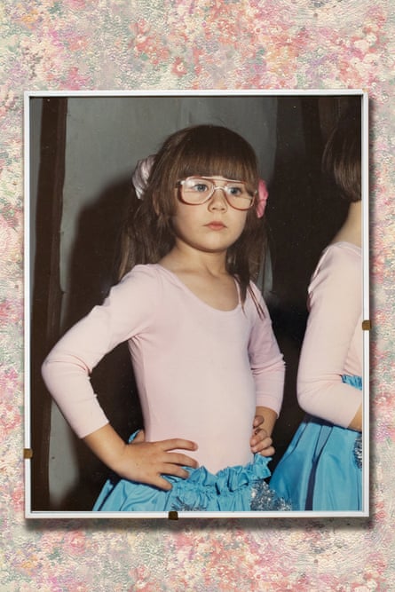 Vanessa as a young girl wears large glasses; she appears to be in a dance class and wears a pale pink leotard-style top and pale blue skirt, and has long, thick hair with a fringe. She stands with her hands on her hips.