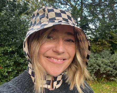 A woman wearing an L-Hood checked rain hat smiles outdoors in front of greenery