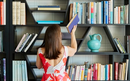 A woman with brown hair is returning the book she was reading to its place on the shelf.