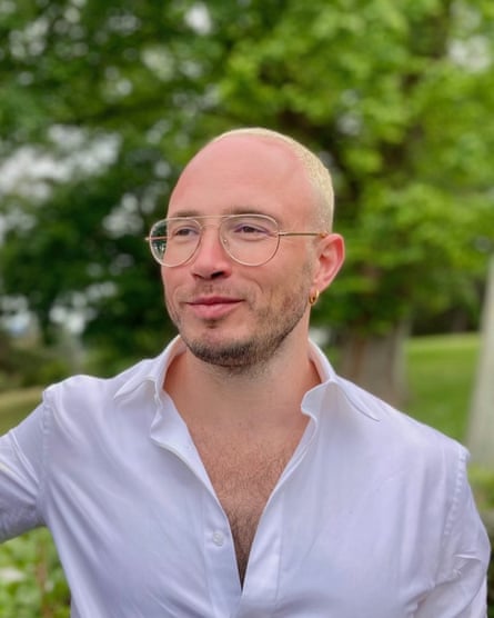 A man with cropped short hair and glasses in an partially-buttoned shirt. 