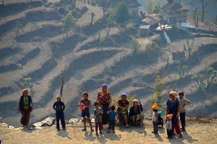 Small group of men, women and children with steeply terraced hill and traditional houses in background