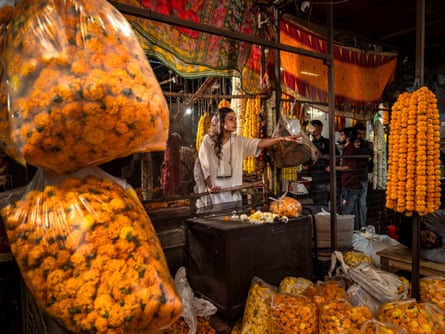 A woman stands behind a stall with dried corn hanging in the foreground.