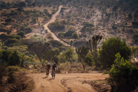 Two cyclists on a dusty dirt trail through vegetation