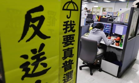 A journalist at her computer seen from behind with two fluorescent-yellow banners in Chinese in the foreground, one with an umbrella