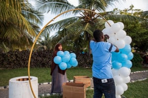A woman carries blue balloons and a man attaches them to a large metal hoop