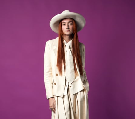 Harris Reed wearing a cream suit, shirt, tie and hat, against a purple background