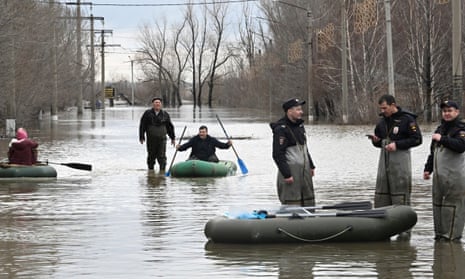 Police officers stand guarding an area as people use rubber boats in a flooded street after part of a dam burst, in Orsk, Russia.