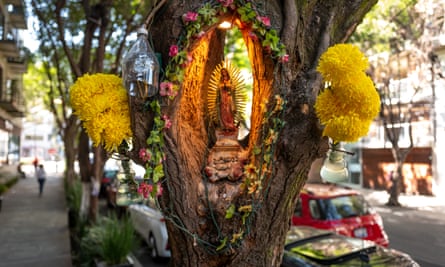 A colourful shrine inside a carved hole in a tree on a street.