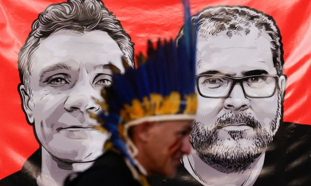 An Indigenous activist walks past pictures of Dom Phillips and Bruno Pereira.