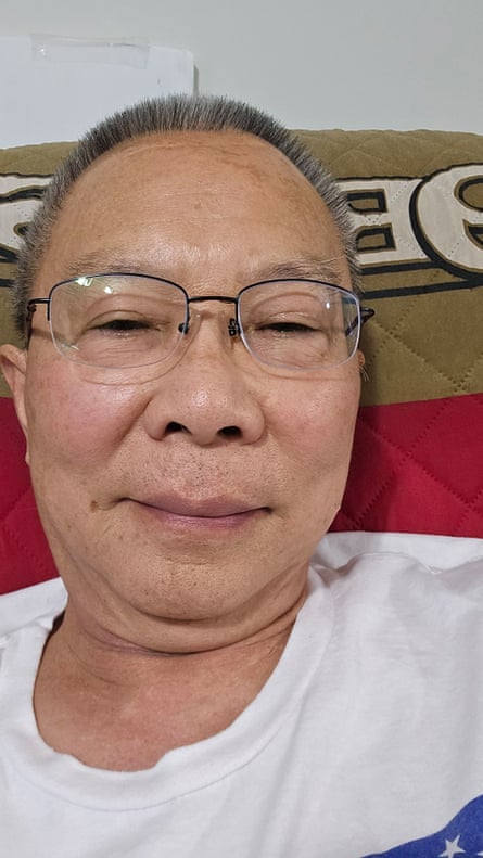 Man in glasses and T-shirt sitting on couch, taking a selfie and smiling.