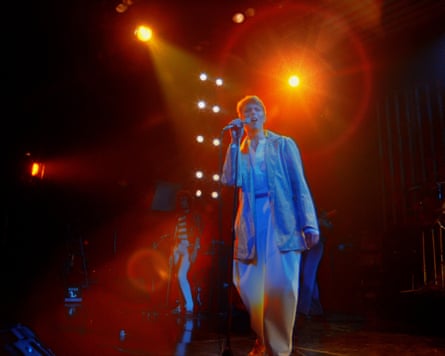 Bowie, lit in blue, singing into a mic against orange spotlights