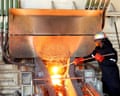 a worker in full protective gear stokes a white hot furnace at a smelting plant