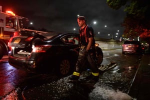 A firefighter walks past cars as flood water is pumped from a nearby house in Brooklyn
