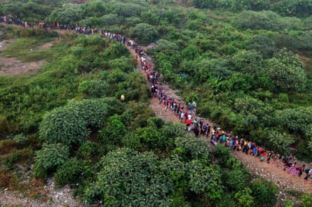 An aerial shot of a long row of people walking through the jungle