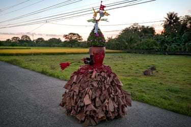 Image 23: A man wearing a wide-bottomed dress made of dried banana leaves and a colourful headdress, holding a whip