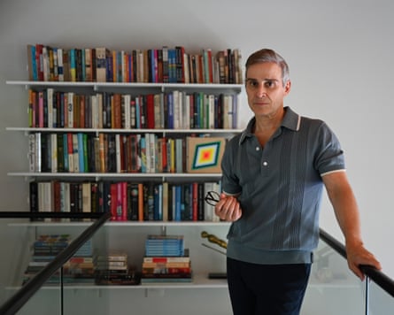Frank Spinelli stands on a raised internal balcony area in his home, with a stacked bookshelf in the background