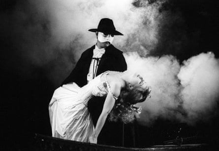 A man in evening dress with a white mask on carrying an unconscious woman in evening dress