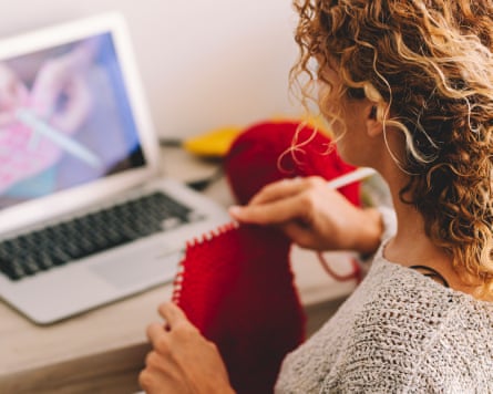 Young woman knitting wool using needle while watching online tutorial on laptop at home.