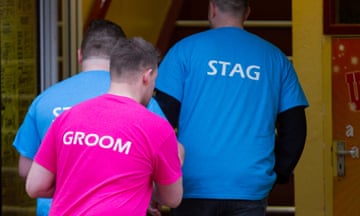 Man dressed in pink t-shirt with 'groom' on the back and two men in blue t-shirts with 'stag' on the back
