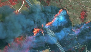 A huge fire rips across a main road; the smoke above is so thick the ground is barely visible.