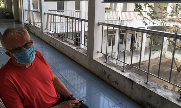 Graham Craddock wears a blue mask and sits on a balcony in Vietnam