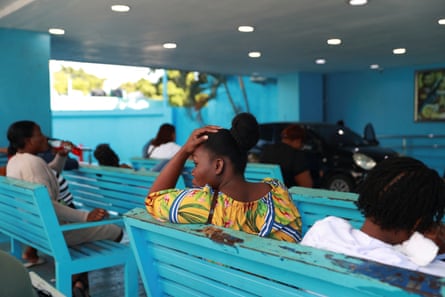 Women sit on blue wooden benches in a hospital waiting room