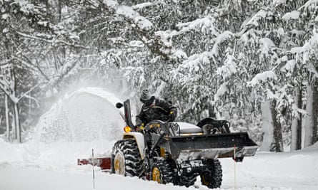 A person removing snow from a snowy road with a backhoe loader.