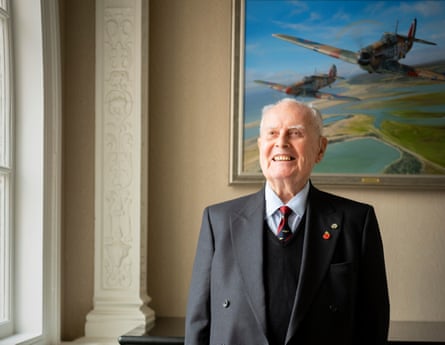 Colin Bell standing in front of a painting of planes at the RAF Club in London.