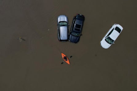 A person in a canoe passes cars partially submerged by flood waters from recent rain storms