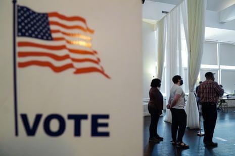 People wait in line to vote as a 'Vote' sign with an American flag can be seen in the foreground.