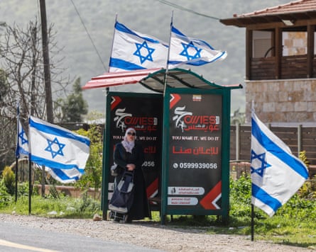 A Palestinian woman waits at a bus stop decked out with Israeli flags