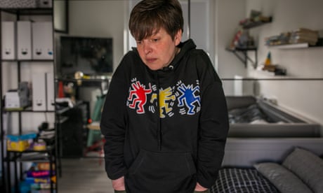 An unhappy-looking woman in a hoody stands with her shoulders hunched and her hands in her pockets