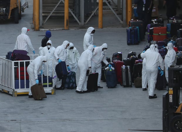 Workers dressed in hazmat suits take the luggage off the Zaandam cruise ship.