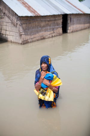 A woman stands in floodwaters clutching a bag to her chest