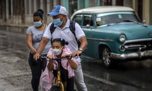 A girl wearing a mask against the spread of the new coronavirus is carried on the bicycle by her father in Havana, Cuba, Tuesday, Oct. 6, 2020.