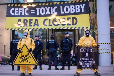 Activists wearing yellow hazmat suits protest outside the office