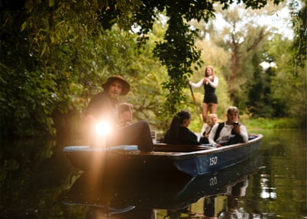 A man with a torch and people with bat detectors sail in the evening light in a punt