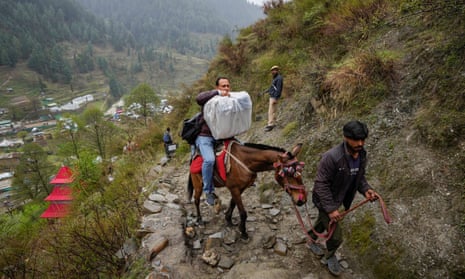 A man transports an electronic voting machine on a pony as election officials walk to a polling booth in a remote mountain area on the eve of the first round of voting at Dessa village in Doda district, Jammu and Kashmir, India, 18 April.
