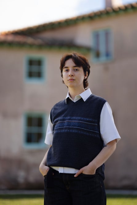 A student poses in a dark vest and white shirt in front of a building